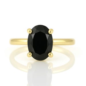 May include: A gold ring with a black oval gemstone. The ring is set with four prongs and has a polished finish.