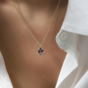 May include: A gold chain necklace with a purple oval gemstone pendant.