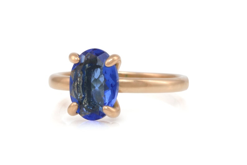 Op de afbeelding: Een gouden ring met een grote ovale blauwe edelsteen.