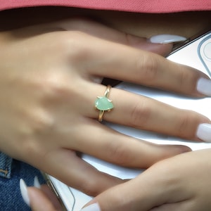 以下が含まれることがあります： 梨の形をした緑色の宝石がついた金の指輪。指輪は人の指にはめられています。