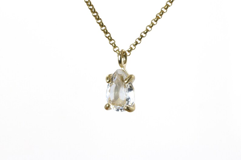 May include: A gold chain necklace with a clear pear-shaped gemstone pendant.
