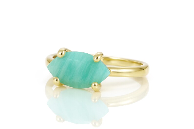 K&ouml;nnte beinhalten: Ein goldener Ring mit einem hellgr&uuml;nen Edelstein, der in einer Zargenfassung gefasst ist. Der Edelstein hat eine Marquise-Form und ein gestreiftes Muster.