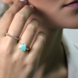 Könnte beinhalten: Ein goldener Ring mit einem hellblauen dreieckigen Edelstein. Der Ring wird am Zeigefinger einer Hand getragen.