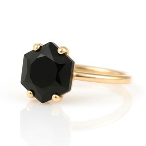 May include: A gold ring with a black octagonal gemstone. The ring is simple and elegant.