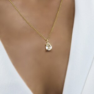 May include: A gold chain necklace with a teardrop-shaped clear gemstone pendant.
