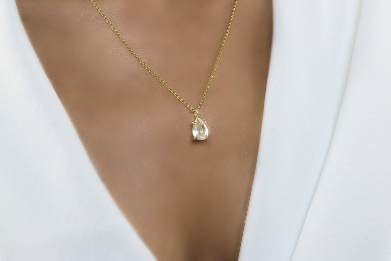 May include: A gold chain necklace with a teardrop-shaped clear gemstone pendant.