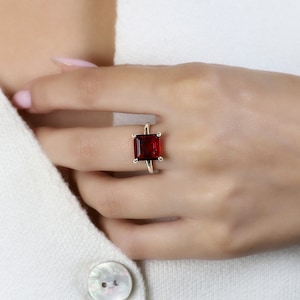 May include: A gold ring with a large, square, red gemstone.