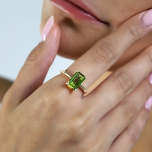 May include: A gold ring with a green gemstone. The ring is on a person's finger.
