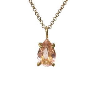 May include: A delicate gold chain necklace with a pear-shaped pink gemstone pendant.