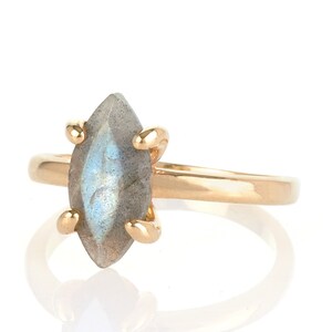 Puede incluir: Un anillo de oro con una piedra de labradorita en forma de marquesa. La piedra gris-azul est&aacute; sujeta por cuatro garras de oro. La banda del anillo es de oro pulido. Joyer&iacute;a.