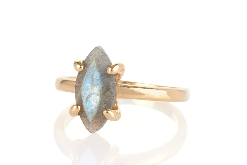 Puede incluir: Un anillo de oro con una piedra de labradorita en forma de marquesa. La piedra gris-azul est&aacute; sujeta por cuatro garras de oro. La banda del anillo es de oro pulido. Joyer&iacute;a.