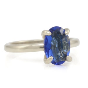 Op de afbeelding: Een zilveren ring met een blauwe ovale edelsteen in een kraalbezetting.