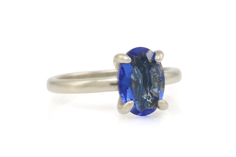 Op de afbeelding: Een zilveren ring met een blauwe ovale edelsteen in een kraalbezetting.