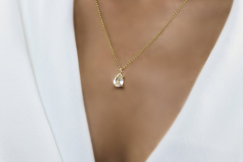 May include: A delicate gold chain necklace with a pear-shaped clear gemstone pendant.