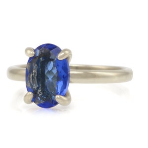 Op de afbeelding: Een zilveren ring met een grote, ovale blauwe edelsteen in een klauwsetting.