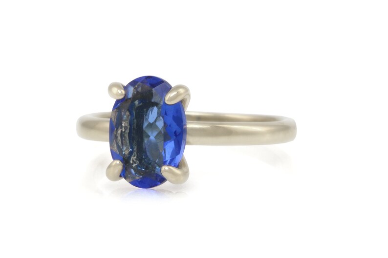 Op de afbeelding: Een zilveren ring met een grote, ovale blauwe edelsteen in een klauwsetting.