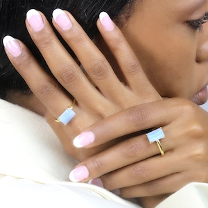 May include: Two gold rings with light blue rectangular stones. The rings are on a person's fingers.