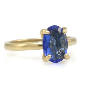 Op de afbeelding: Een gouden ring met een grote, ovale blauwe edelsteen. De ring is gezet met vier griffen.