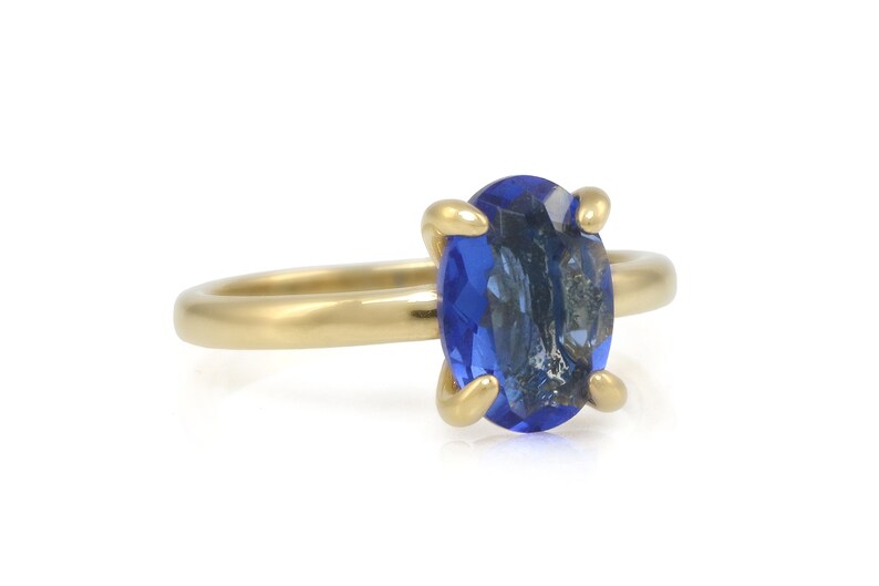Op de afbeelding: Een gouden ring met een grote, ovale blauwe edelsteen. De ring is gezet met vier griffen.