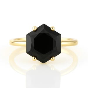 May include: A gold ring with a black octagonal gemstone. The ring is set with small gold accents around the gemstone.