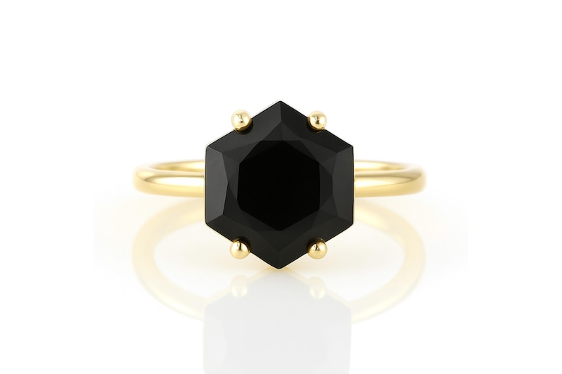 May include: A gold ring with a black octagonal gemstone. The ring is set with small gold accents around the gemstone.