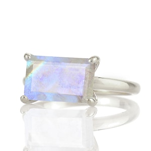 May include: A silver ring featuring a large, rectangular, iridescent moonstone.