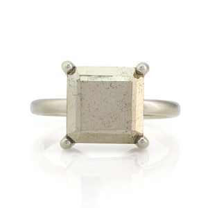 Puede incluir: Un anillo de plata con una piedra cuadrada de color gris claro.