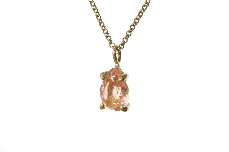 May include: A gold chain necklace with a pear-shaped pink gemstone pendant.