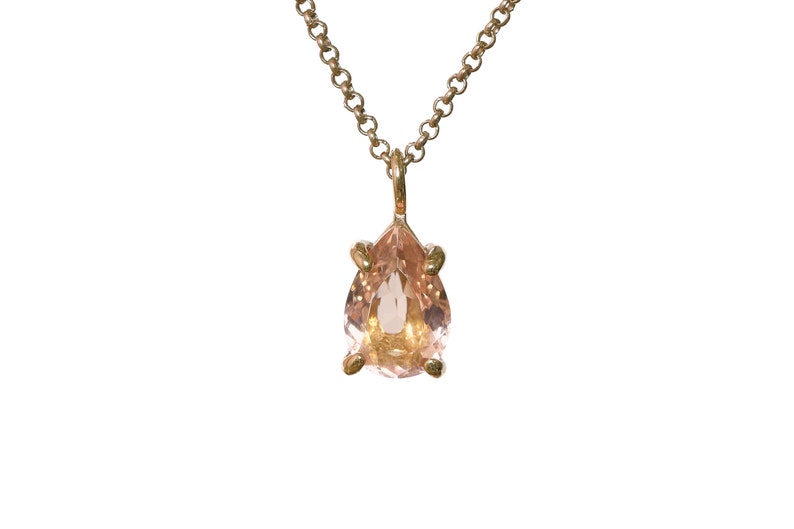 May include: A delicate gold chain necklace with a pear-shaped pink gemstone pendant.