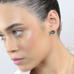 Peut inclure: Une femme portant une chemise blanche avec un collier en or et une paire de boucles d'oreilles clous en pierres précieuses bleues et vertes.