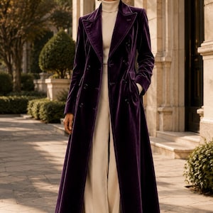 May include: A long, deep purple velvet coat featuring a double-breasted button closure, wide lapels, and side pockets. The coat is worn over a cream-colored ribbed turtleneck sweater and matching wide-leg trousers with a clean, tailored finish.