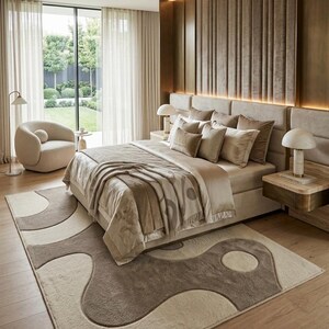 Pu&ograve; includere: Una camera da letto con un letto dotato di biancheria beige e un plaid, posizionato su un grande tappeto con un motivo organico astratto marrone e crema. La stanza include un'alta testiera imbottita, due comodini con lampade e una sedia.