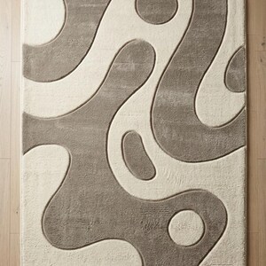 Pu&ograve; includere: Un tappeto rettangolare caratterizzato da una texture a pelo alto e basso con un design bicolore. Il motivo &egrave; composto da forme organiche fluide e cerchi color tortora su uno sfondo color crema, creando un effetto di rilievo e profondit&agrave;.