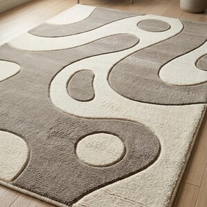Pu&ograve; includere: Un tappeto rettangolare caratterizzato da una texture a pelo alto e basso con un design bicolore color crema e tortora. La superficie presenta un motivo astratto di linee curve fluide e forme circolari che creano un effetto in rilievo.