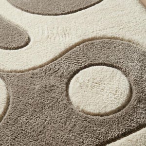 Pu&ograve; includere: Un tappeto rettangolare caratterizzato da una texture a pelo alto e basso con un motivo ripetitivo di grandi cerchi in rilievo e forme curve. Il design &egrave; composto da una palette di colori neutri con sezioni alternate di fibre color crema e tortora.