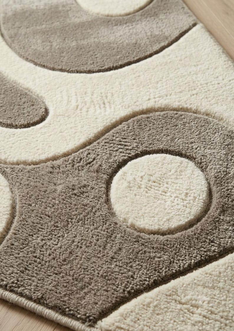 Pu&ograve; includere: Un tappeto rettangolare caratterizzato da una texture a pelo alto e basso con un motivo ripetitivo di grandi cerchi in rilievo e forme curve. Il design &egrave; composto da una palette di colori neutri con sezioni alternate di fibre color crema e tortora.
