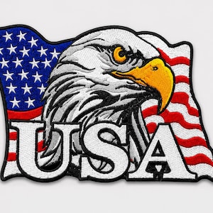 Könnte beinhalten: Ein gestickter Aufnäher mit einem Weißkopfseeadler-Kopf mit gelbem Schnabel und Auge, platziert vor einer wehenden amerikanischen Flagge. Die Buchstaben USA sind in großen weißen Großbuchstaben mit schwarzer Umrandung im unteren Bereich gestickt.