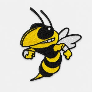 May include: An embroidered patch featuring a cartoon hornet with a yellow and black striped body, a large black eye, and white wings. The hornet is depicted in a dynamic pose with its arms raised, showcasing detailed stitching and bold colors.