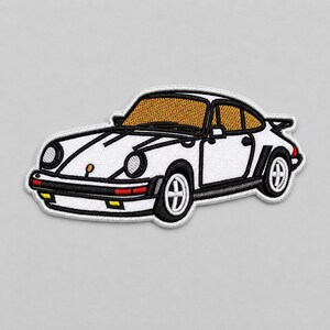 Op de afbeelding: Een geborduurde patch van een witte sportwagen met zwarte details, ronde koplampen en goudkleurige ramen. Het ontwerp bevat een achterspoiler, zwarte wielen met witte spaken en kleine rode en gele accentverlichting op de voorbumper.