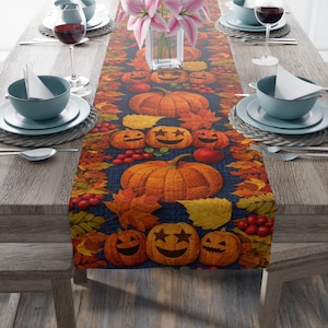 May include: A rectangular table runner featuring a dark blue background with a repeating pattern of orange pumpkins, jack-o'-lanterns with star-shaped eyes, red berries, and autumn leaves in shades of yellow, orange, and deep red.