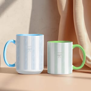 Puede incluir: Dos tazas de cerámica con rayas verticales. La taza más alta tiene un asa e interior azul claro con exterior de rayas azules. La taza más baja tiene un asa e interior verde con exterior de rayas verdes. Ambas tazas llevan el nombre Samantha impreso.