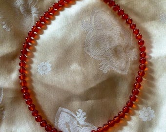 May include: A necklace made of carnelian beads with a gold clasp. The beads are a deep orange color and are strung on a thin gold chain.