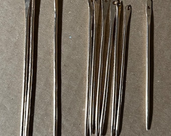 May include: A set of 12 silver knitting needles, with a variety of sizes, arranged in a row on a brown surface.