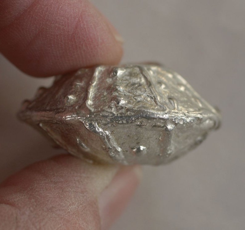 May include: A silver, irregularly shaped, metal pendant with a textured surface.