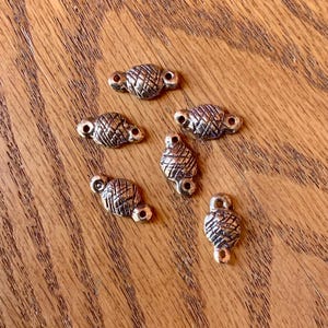 May include: Six gold-toned metal connector charms with a textured, woven design. Each charm has two small loops for attaching to jewelry or other crafts.
