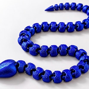 May include: A vibrant blue articulated snake toy featuring a textured, segmented body that curves in an S-shape. The figure has a smooth, pointed head and a tapered tail, with visible 3D-printed layer lines across its entire surface.