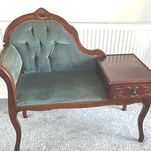 Mesa de teléfono vintage de madera tallada con asiento tapizado capitoné verde.