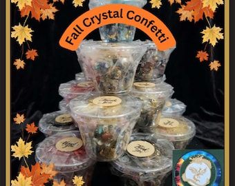 Puede incluir: Una pila piramidal de vasos de plástico transparente llenos de cristales y cuentas variadas, etiquetados como Fall Crystal Confetti. Cada vaso tiene una pegatina circular de Thank You en la tapa. Se ve un pequeño emblema con un fénix dorado.