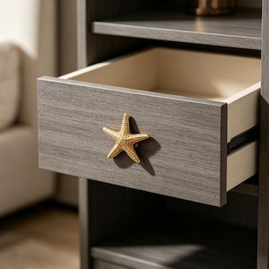 May include: A dark gray wood-grain nightstand featuring a single pull-out drawer with a textured gold-toned starfish knob. The drawer interior is light beige, and the unit includes an open shelf space above and below the drawer section.