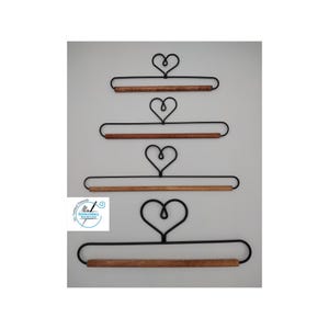 May include: Four black metal wall hangers of varying widths, each featuring a heart-shaped top loop and a horizontal wooden dowel at the base. A circular logo with the text Embroidery Boulevard is visible on the left side of the image.